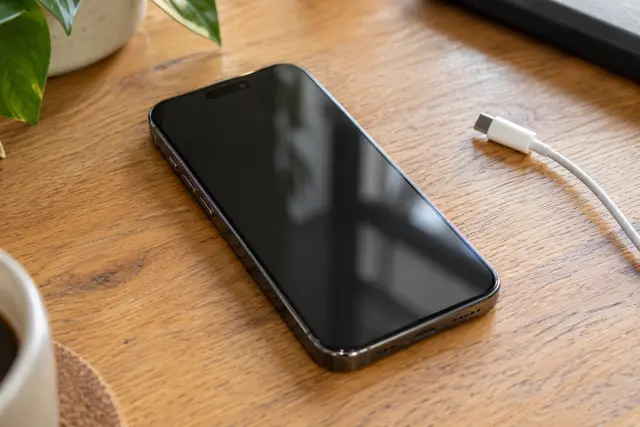 Ahşap masada iPhone’un ön yüzü ve şarj kablosu